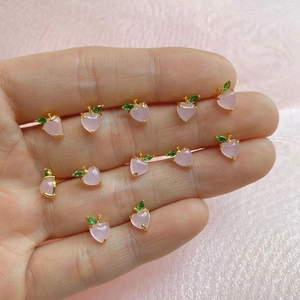 Macro shot of mini pink peach stud earrings with green zircon leaves on golden base
