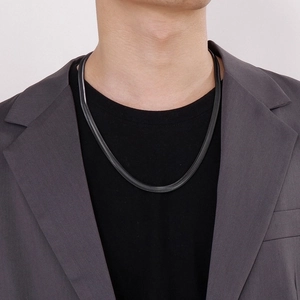 Detail view of a black flat snake bone chain necklace worn by a male model in a grey suit