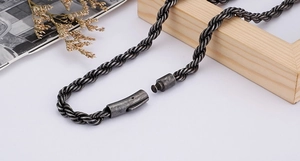 Macro shot of dark metal twisted rope chain with plug-in clasp and rustic background