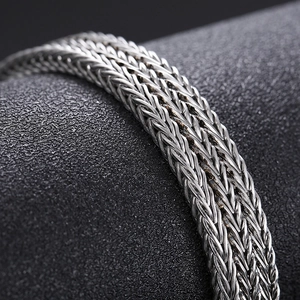 Macro detail of silver woven titanium steel chain with intricate mesh pattern on black surface