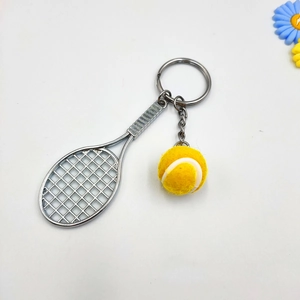Close-up of a silver metal tennis racket keychain with a yellow mini felt ball on white background