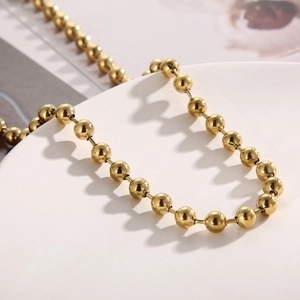 Macro shot of a polished golden stainless steel bead chain necklace on a white display