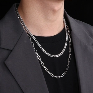 Detail of layered silver titanium steel cuban and paperclip chain on grey suit