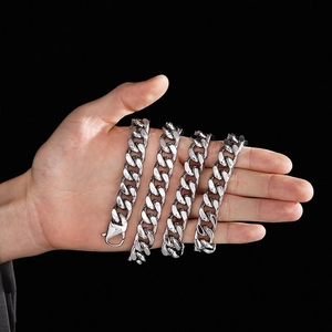 Detail of 14mm silver stainless steel Cuban link chains held in palm on black background