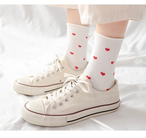 Close-up of white cotton crew socks with red heart patterns worn with canvas shoes