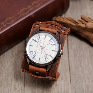 Detail shot of a vintage brown leather cuff watch with a white dial on a rustic wood surface
