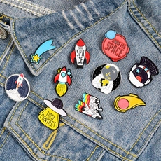 Space enamel pins set with astronaut and rocket designs pinned on a blue denim jacket