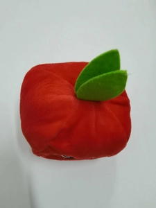Top view of red apple-shaped plush dog toy with green fabric leaves on white background