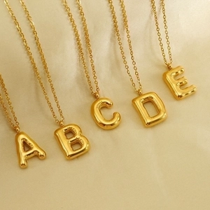 Detail of five 18K gold-plated initial necklaces on beige silk background