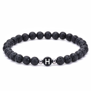 Macro detail of natural lava stone beads and white letter H charm on elastic bracelet