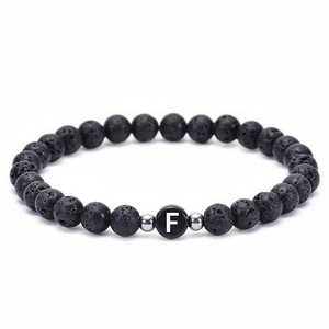 Macro detail of natural black lava stone beads with a white letter F on the center bead