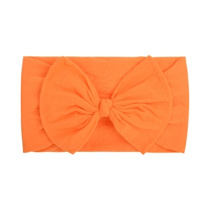 Detail of soft nylon orange baby headband featuring a large knitted bow on white background
