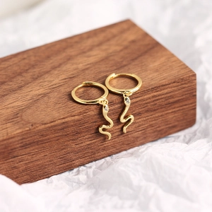 Close-up of golden snake hoop earrings with small zircon studs on a wooden stand