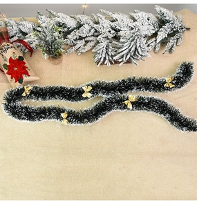 Detail showing dark green Christmas garland with white tips and golden bows on rustic burlap