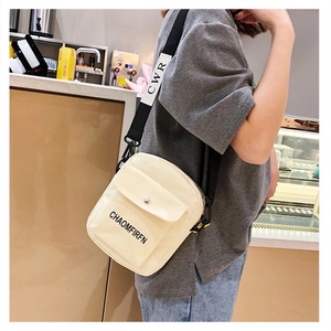 Detail of off-white canvas crossbody bag with adjustable wide strap in a cafe setting