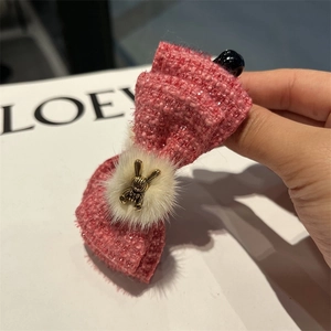 Detail of pink tweed bow hair clip with white fur ball and golden rabbit pendant
