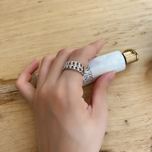 Close-up of a double-layered silver chain ring on finger against a wooden background