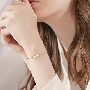 Detailed view of a gold cross bracelet with a delicate O-chain on a woman wrist