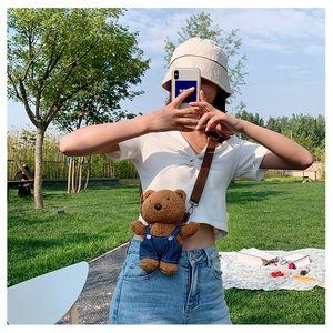 Close-up of brown plush bear crossbody bag with denim overalls in a sunny picnic scene