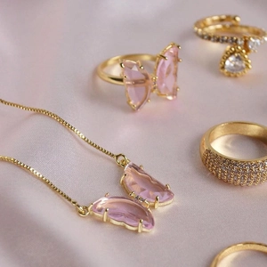 Detail of gold-plated butterfly jewelry set with pink stones on pink satin fabric