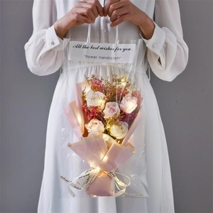 Pink soap roses and carnation bouquet in transparent bag with LED lights and ribbon