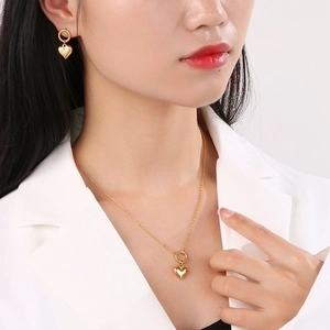 Elegant gold heart pendant necklace and earrings set worn by a model in a white suit