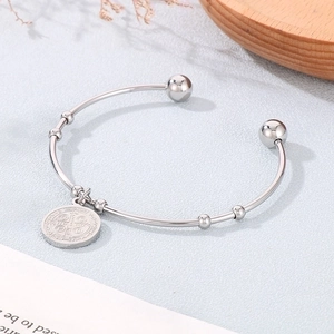 Detail of silver cuff bracelet featuring a Saint Benedict coin pendant on a textured surface