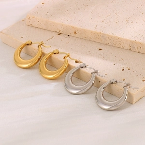 Polished gold and silver geometric C-shape hoop earrings on minimalist stone display