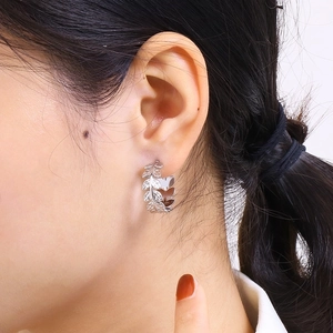 Close-up of silver wheat leaf C-shaped titanium steel earrings worn on a model's ear