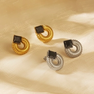 Close-up of gold and silver stud earrings featuring black square stones and spiral texture