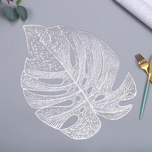 Detail of silver monstera leaf placemat with intricate hollowed veins on grey surface