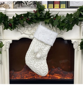 Chaussette de Noël en tricot blanc avec bordure en fourrure et pompons sur la cheminée