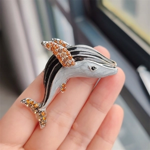 Hand holding a whale brooch with black enamel stripes and orange rhinestones