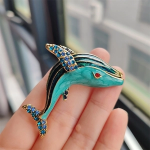 Macro shot of a whale brooch with blue rhinestones and teal enamel details held in hand