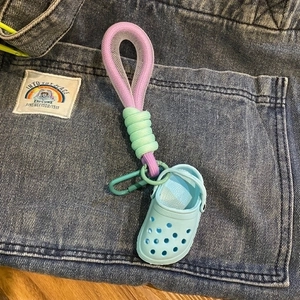 Miniature light blue clog shoe keychain with colorful woven strap on denim background