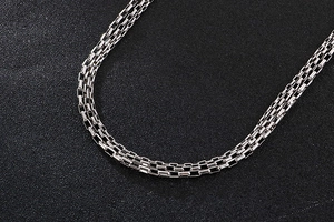 Macro close-up of a silver multi-strand woven metal chain necklace on black background