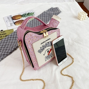 Pink sequin fuel tank shaped handbag with gold chain strap on white fabric background