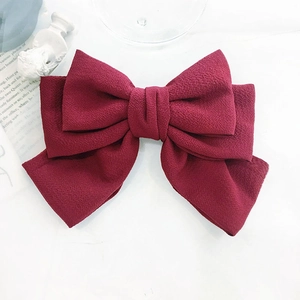 Detail of burgundy bubble gauze bow hair clip made of premium textured fabric on a white surface