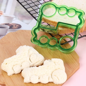 Green plastic train-shaped sandwich cutter mold with bread on a wooden board