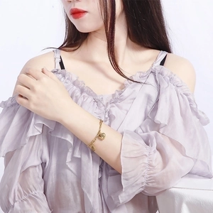 Elegant gold titanium steel bracelet with heart pendant on model's wrist with lilac shirt