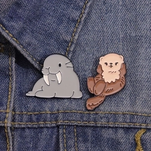 Detailed view of sea otter and walrus enamel pins pinned on a blue denim jacket