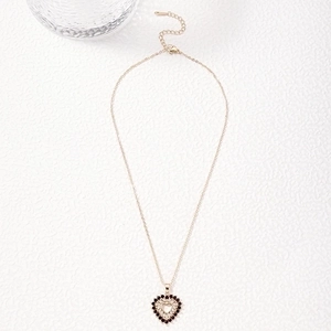 Golden heart pendant necklace with deep red zircon stones on white textured surface
