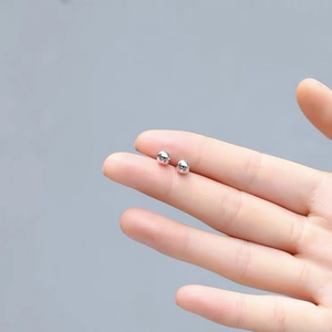 Macro shot of minimalist S999 sterling silver ball earrings resting on a finger