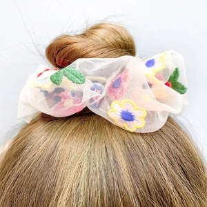 Off-white sheer mesh hair scrunchie with daisy flower embroidery on a hair bun