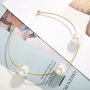 Detailed view of a gold metal choker with three large white pearls on a minimalist background