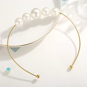 Detail of a gold open collar necklace featuring five graduated white pearls on a minimalist band