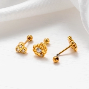 Close-up of gold zircon ear studs with screw ball backs on white silk fabric background