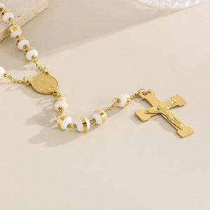 Detailed macro view of 18K gold-plated cross pendant and white beads on a rosary necklace