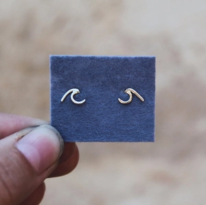 Detailed view of wave-shaped golden earrings held against a neutral blurred background