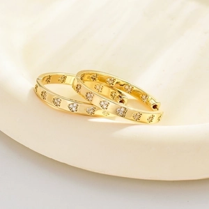 Exaggerated golden hoop earrings with heart-shaped zircon stones on ceramic plate